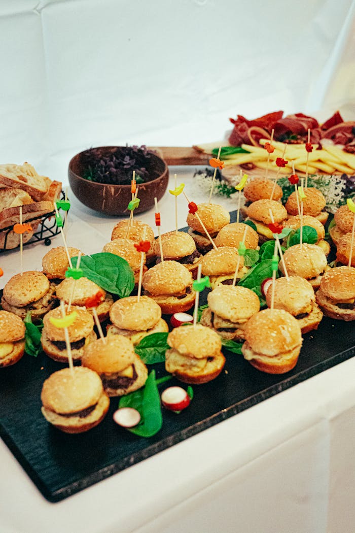 A vibrant display of mini burgers with skewers at a catering event, highlighting festive food presentation.